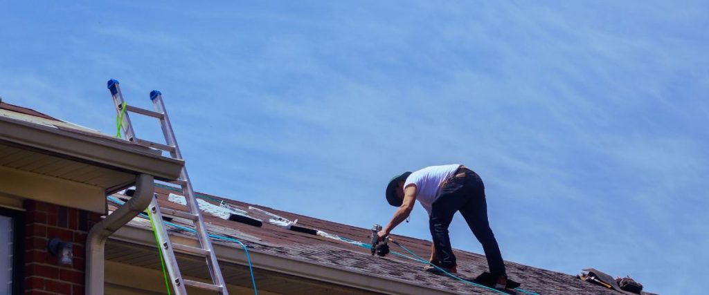 Roofer working on a house roof beside a ladder and gutter